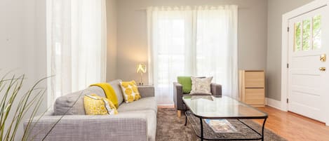 A modern living room with a grey sofa, a glass coffee table, and a small side table with a lamp.