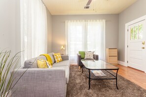 Un salon moderne avec un canapé gris, une table basse en verre et une petite table d’appoint surmontée d’une lampe.