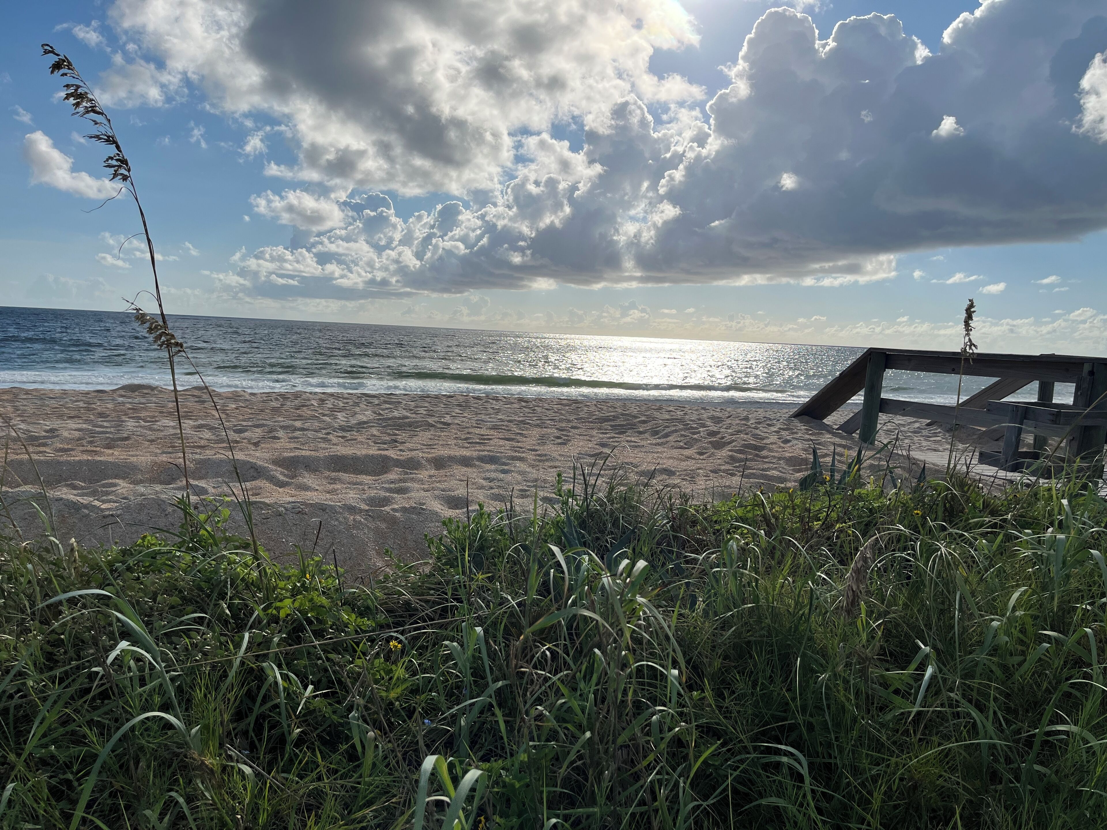 A beach with a wooden structure, waves, and a partly cloudy sky.