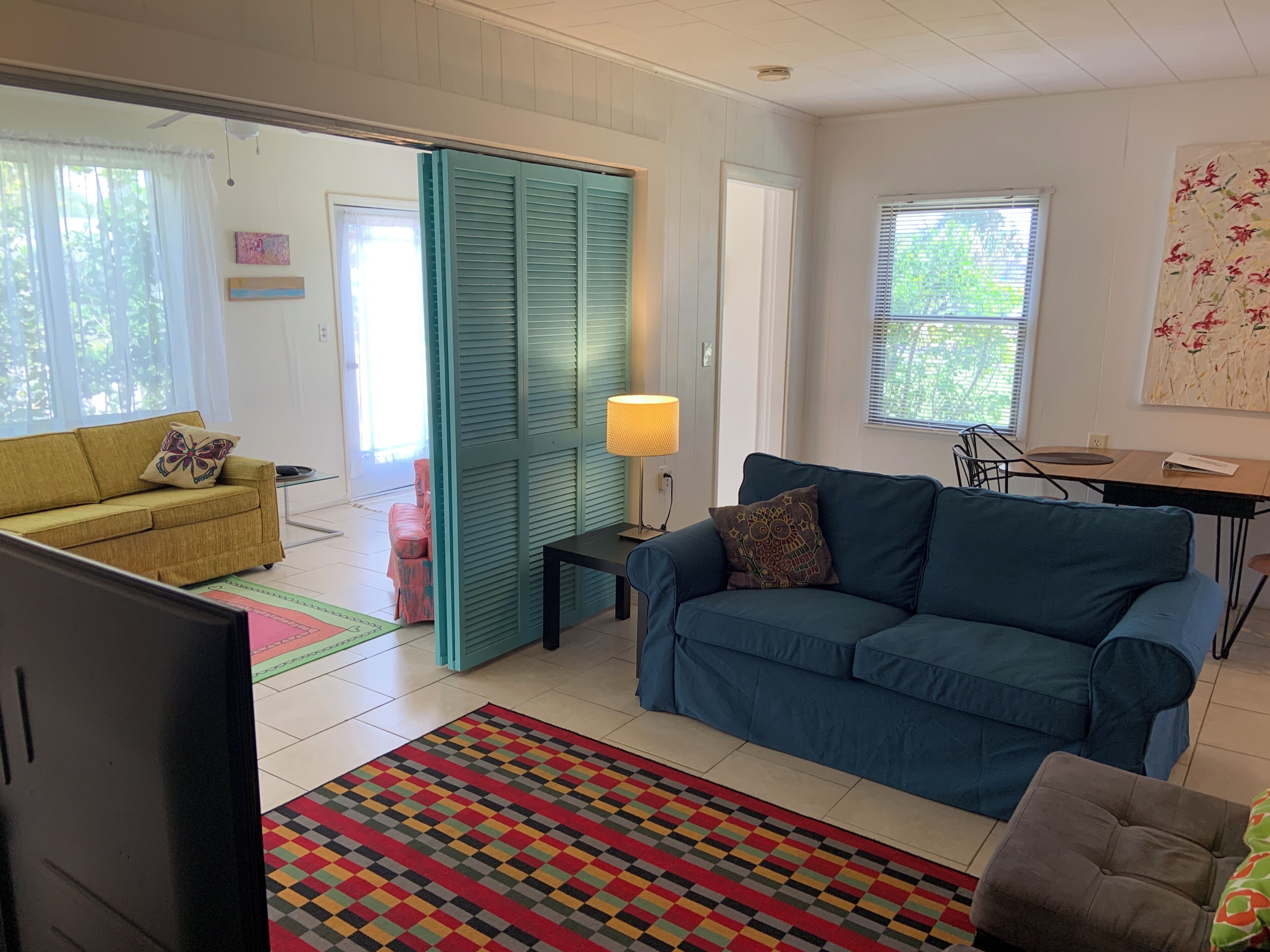 Un salon avec un canapé bleu, un canapé jaune, un tapis à motifs et un mur de séparation de couleur turquoise.