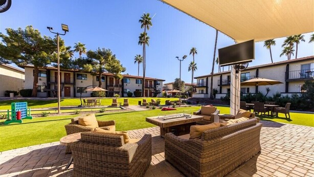 Un espace patio aménagé avec des meubles en osier, un téléviseur à écran plat et une pelouse bien entretenue.