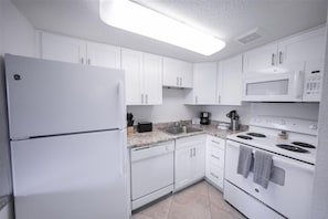A modern kitchen with white cabinets, a refrigerator, a microwave, a stove, and a sink.