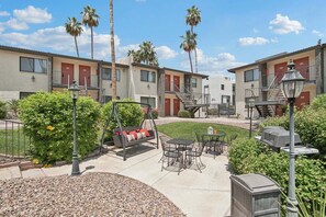 A courtyard with outdoor seating, palm trees, and a building with multiple doors and windows. - 128 1 bedroom, pool, pickleball, hot tub, outdoor grill (Scottsdale)