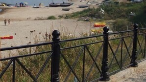 Una playa con barcos, una cerca y edificios al fondo.