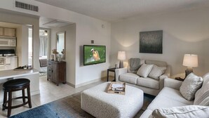 A modern living room with a sofa, ottoman, and a television displaying a golf scene. - 121 Chic Scottsdale Retreat | Heated Pool, Outdoor Lounge & 2 Miles from Old Town! (Scottsdale)