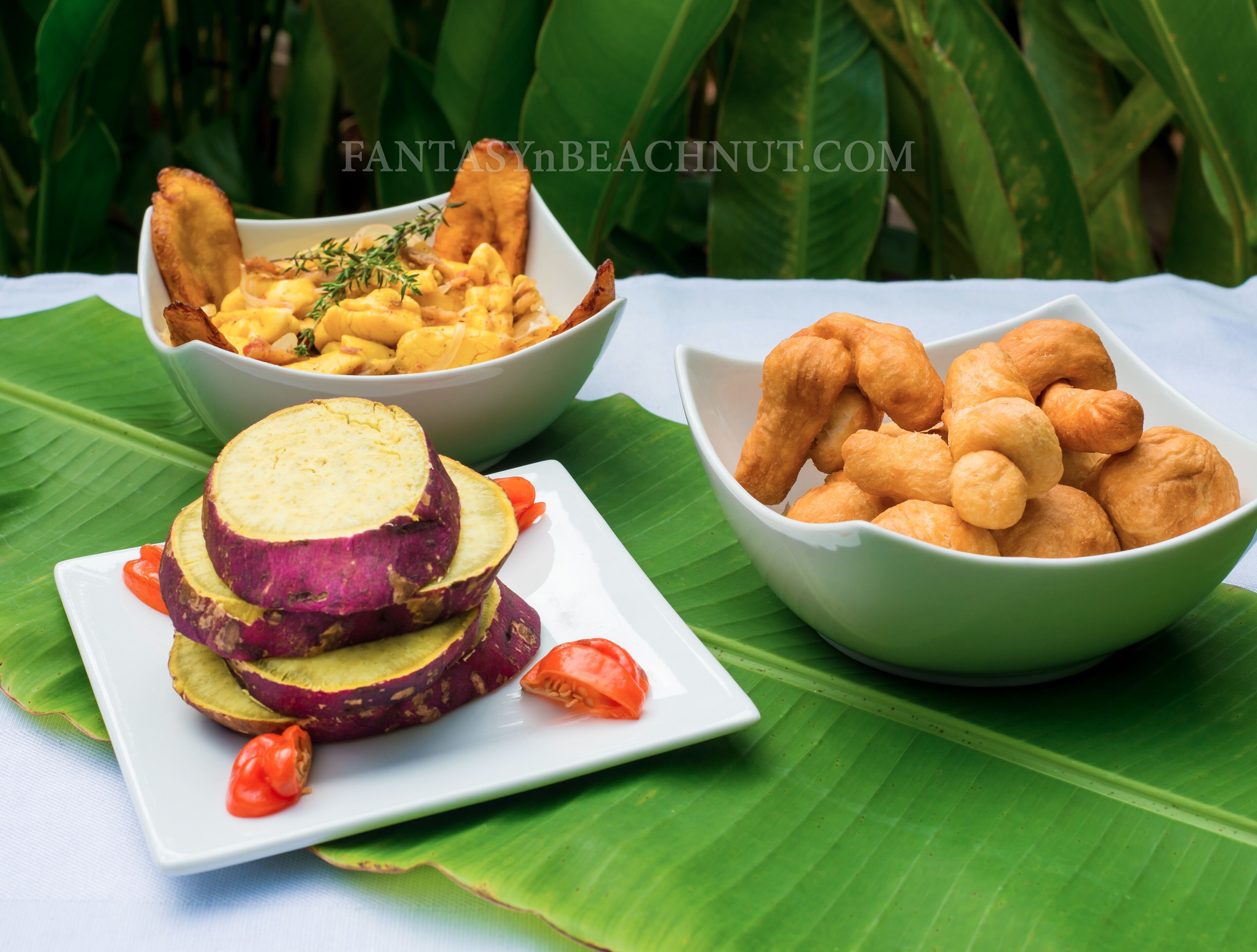 Una mesa con tres cuencos de comida, un plato de batatas en rodajas y una hoja de plátano.