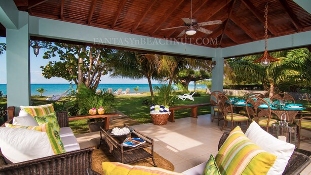 A covered outdoor seating area with wicker furniture, a table with a magazine, and a view of the beach and ocean. - Villa BEACHNUT - ON PRIVATE BEACH IN A GATED COMMUNITY (Rio Bueno)