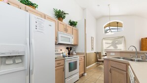 Una cocina moderna con refrigerador, microondas, horno y lavabo. Hay armarios de madera y una ventana con vistas.