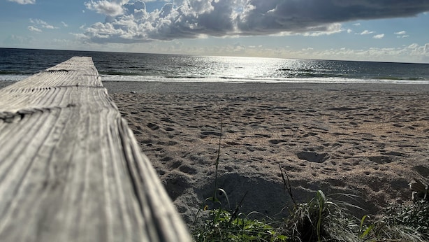 Una passerella di legno che conduce a una spiaggia con vista sull'oceano e un cielo parzialmente nuvoloso.