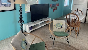 Un soggiorno con televisore, lampada, zona pranzo con sedie e frigorifero.