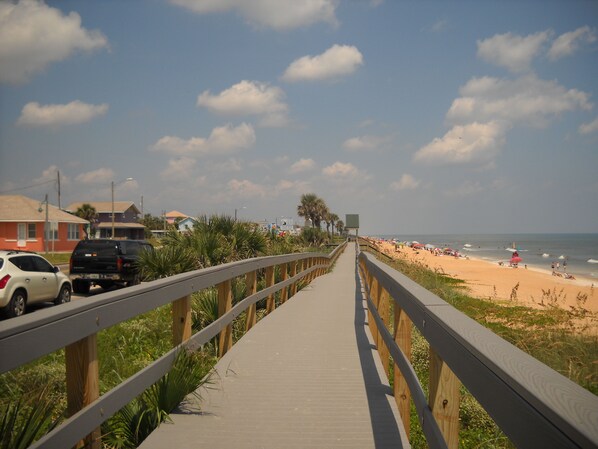 A wooden boardwalk leading to a beach with palm trees and a clear sky.