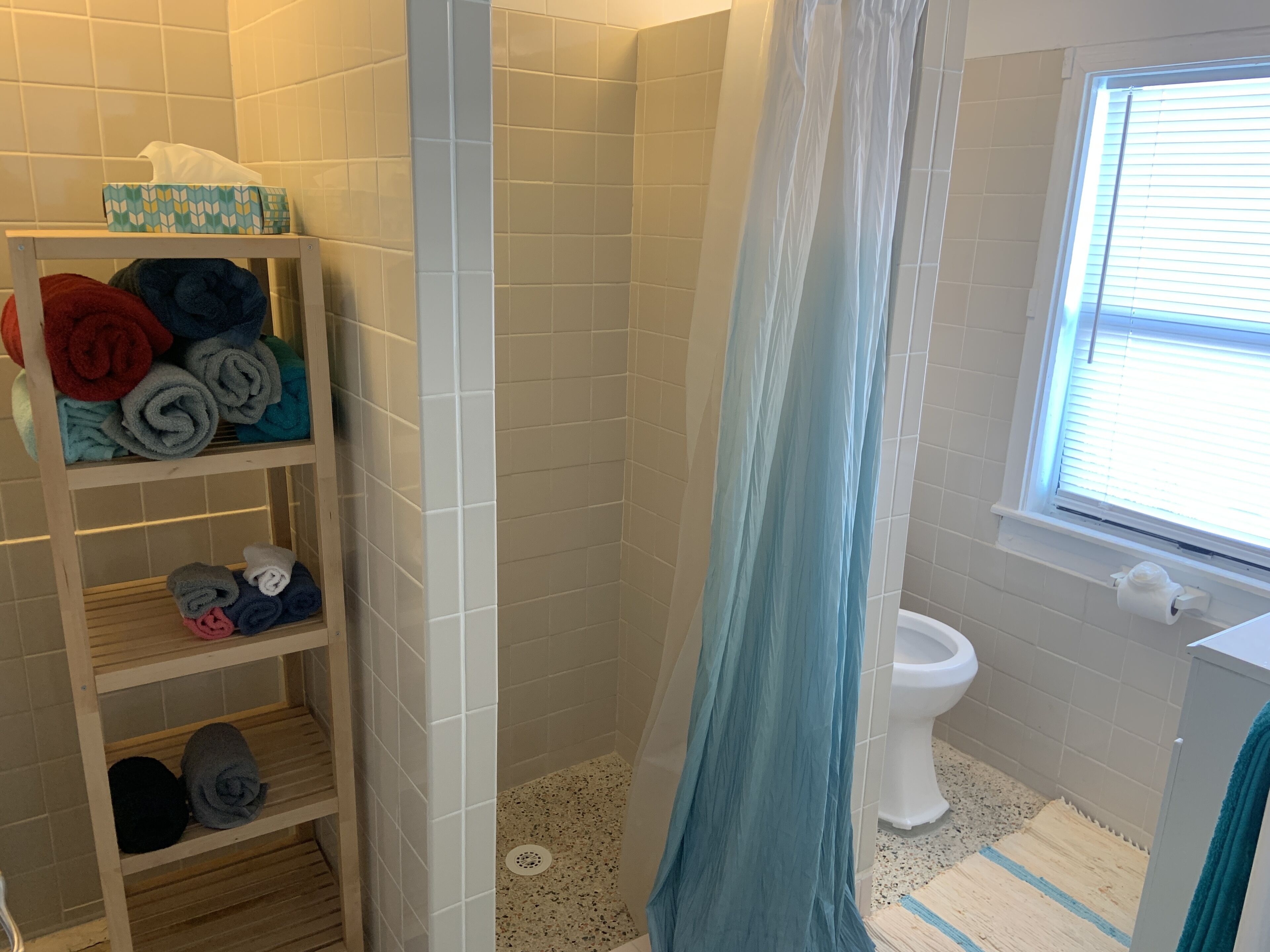 Une salle de bain avec une douche, des toilettes, une fenêtre et une étagère avec des serviettes.