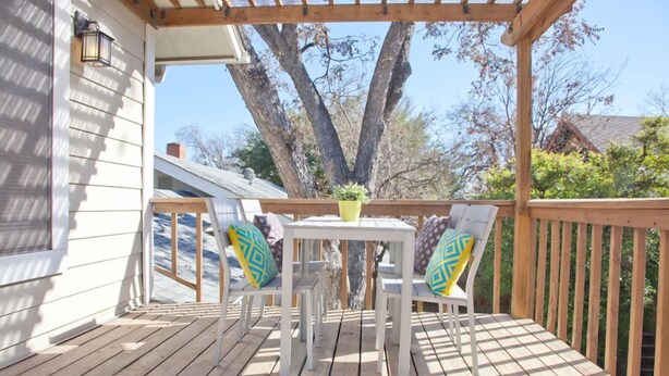 A wooden deck with a white table and two chairs, a yellow flower pot, and a pergola. - Spacious 2 Bedroom in Historic Hyde Park (Austin)