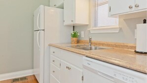 A kitchen with white cabinets, a granite countertop, a built-in dishwasher, and a window with blinds. - Spacious 2 Bedroom in Historic Hyde Park (Austin)