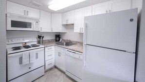 Une cuisine avec des armoires blanches, un four à micro-ondes, une cuisinière, un évier et un réfrigérateur.