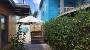 A pathway leading to a house with a blue exterior, a wooden fence, and a white umbrella.