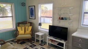 A cozy living room with a television, a small white table, a patterned rug, and a wicker chair.