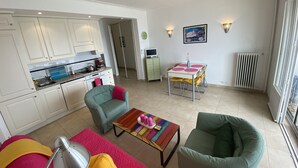 Un salon moderne avec une cuisine en arrière-plan, une table à manger avec des chaises et une grande fenêtre offrant une vue dégagée.