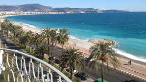 Une route côtière bordée de palmiers, une plage et une vue sur une ville au loin.