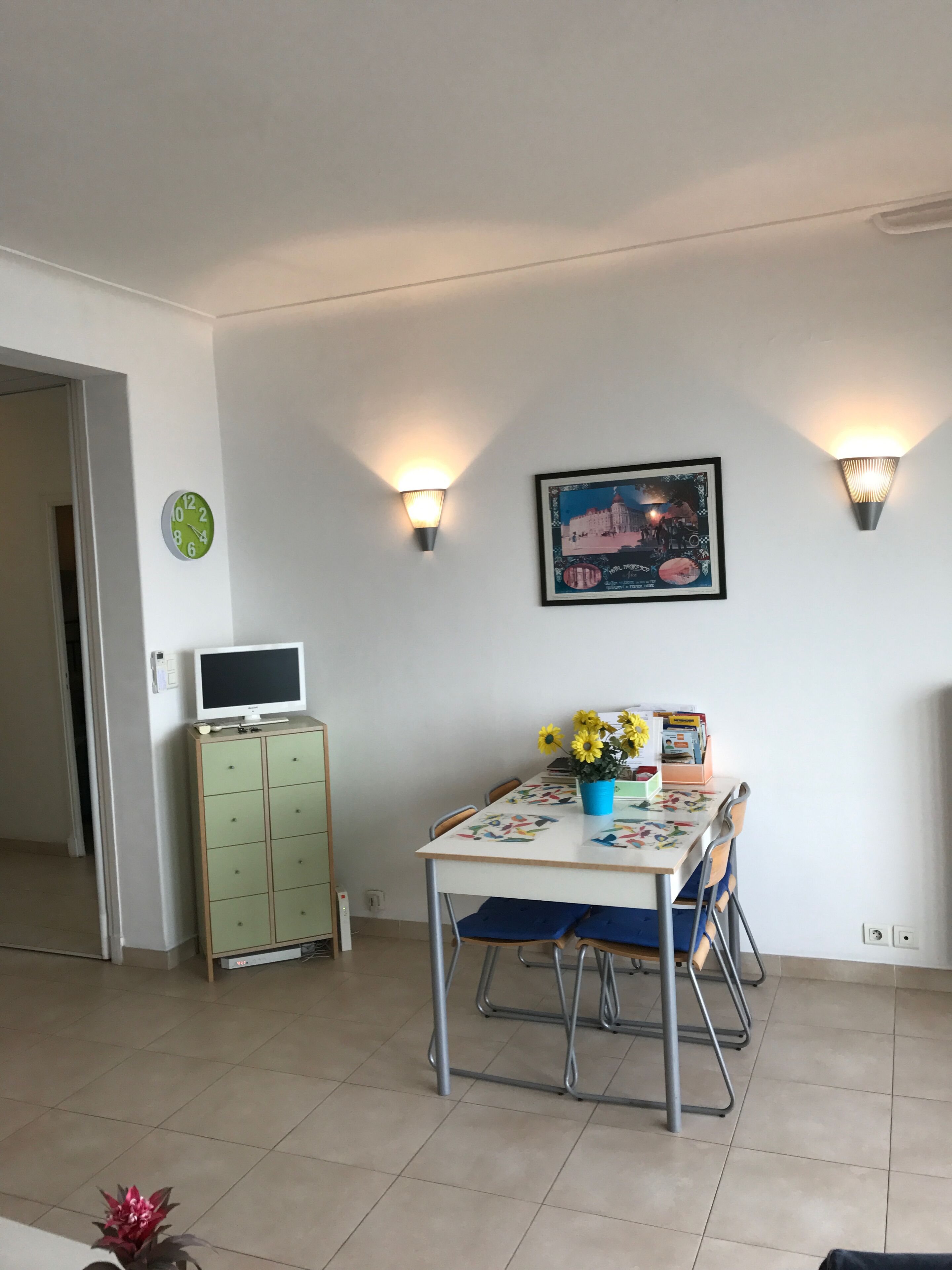 Zona pranzo con tavolo, sedie, un armadio, una sveglia e luci a parete.