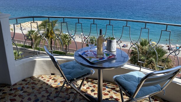 Un balcon donnant sur la mer, une table avec une bouteille et un magazine, et deux chaises.