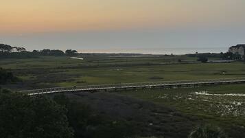 A coastal landscape with a bridge, open fields, and a body of water reflecting the sky.