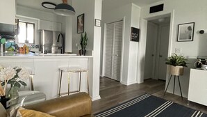 Una cocina moderna con refrigerador, estufa y comedor. Cuenta con ventilador de techo, barra y una sala de estar con sofá y alfombra.