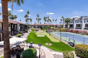 A golf course with a putting green, tennis courts, and a patio area with outdoor seating.
