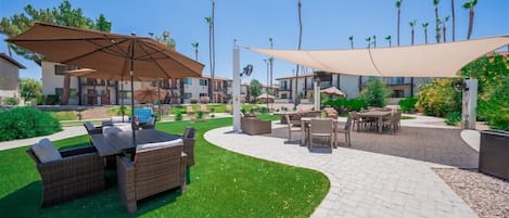 A patio area with outdoor furniture, including a table and chairs, surrounded by palm trees and a clear sky.