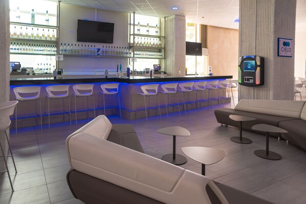 A modern bar area with a counter, multiple bar stools, and a seating area with sofas and small tables. - HIGH FLOOR BEACHFRONT CONDO WITH OCEAN/CITY VIEW IN PRIME LOCATION (Carolina)