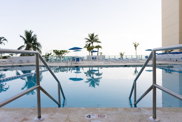 A swimming pool with a 4 ft depth limit sign, surrounded by lounge chairs and palm trees.