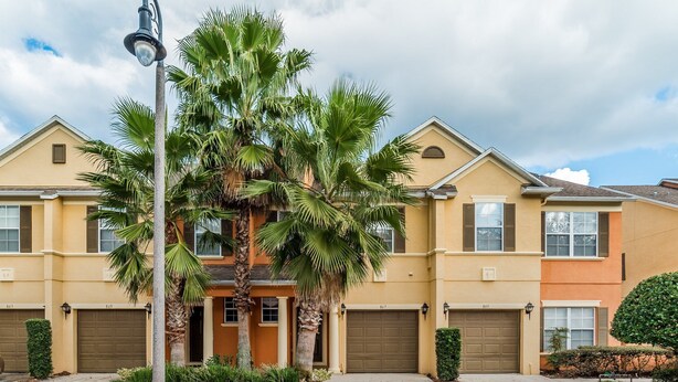 A two-story residential building with a beige facade, a central entrance with a small porch, and a palm tree in the front yard.