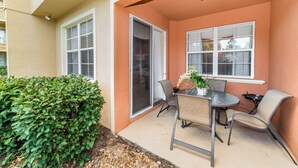 An outdoor patio area with a table and chairs, a potted plant, and a large window with blinds.
