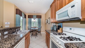 A kitchen with granite countertops, a gas stove, a microwave, and a dining area with a table and chairs.
