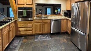 A modern kitchen with wooden cabinets, stainless steel appliances, and a stone tile floor. - A-Frame of Mind in the Smoky's, a mountain retreat. (Whittier)