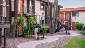 A multi-story building with external staircases, palm trees, and a gravel pathway. - 120 Living in Ultimate Comfort | Pool, Lounge & Full Kitchen Suite! (Scottsdale)