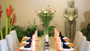 A dining table with a vase of flowers, a Buddha statue, and a unique wooden base.
