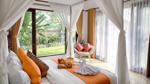 A spacious bedroom with a large bed, a wicker chair, and a view of the garden.