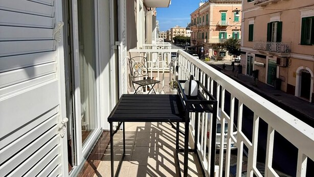 Un balcon avec une table et des chaises, une balustrade blanche et des bâtiments en arrière-plan.