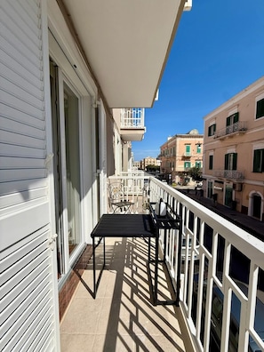 Ein Balkon mit Tisch und Stühlen, einem weißen Geländer und Gebäuden im Hintergrund.
