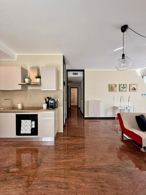 A modern kitchen with integrated appliances, a dining area with a red sofa, and a hallway leading to another room.
