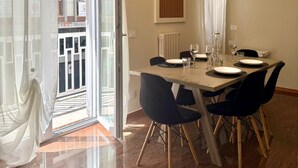 Un coin repas avec une table dressée pour quatre personnes, une porte-fenêtre coulissante et une vue sur un bâtiment à l’extérieur.