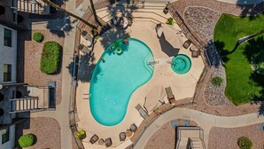 An aerial view of a swimming pool surrounded by lounge chairs, a small deck, and a landscaped area with shrubs and a lawn.