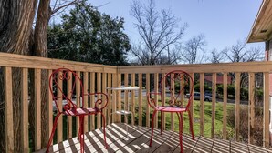 Una terraza de madera con barandilla, dos sillas rojas y una pequeña mesa.