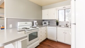 Una cocina moderna con electrodomésticos blancos, suelo de madera y ventana con persianas.