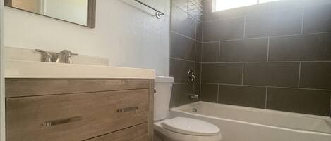 Une salle de bain avec un meuble-lavabo en bois, des toilettes blanches, une baignoire et une douche.
