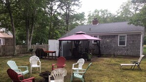 A backyard with a covered patio, outdoor furniture, and a wooden fence. - Quaint Cape Cod Cottage close to all nantucket sound beaches, and RT28 Fun  (South Yarmouth)