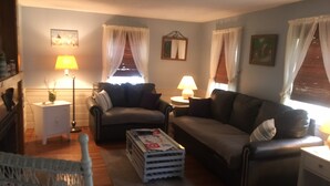 A living room with a sofa, two side tables, a lamp, and a window with curtains. - Quaint Cape Cod Cottage close to all nantucket sound beaches, and RT28 Fun  (South Yarmouth)