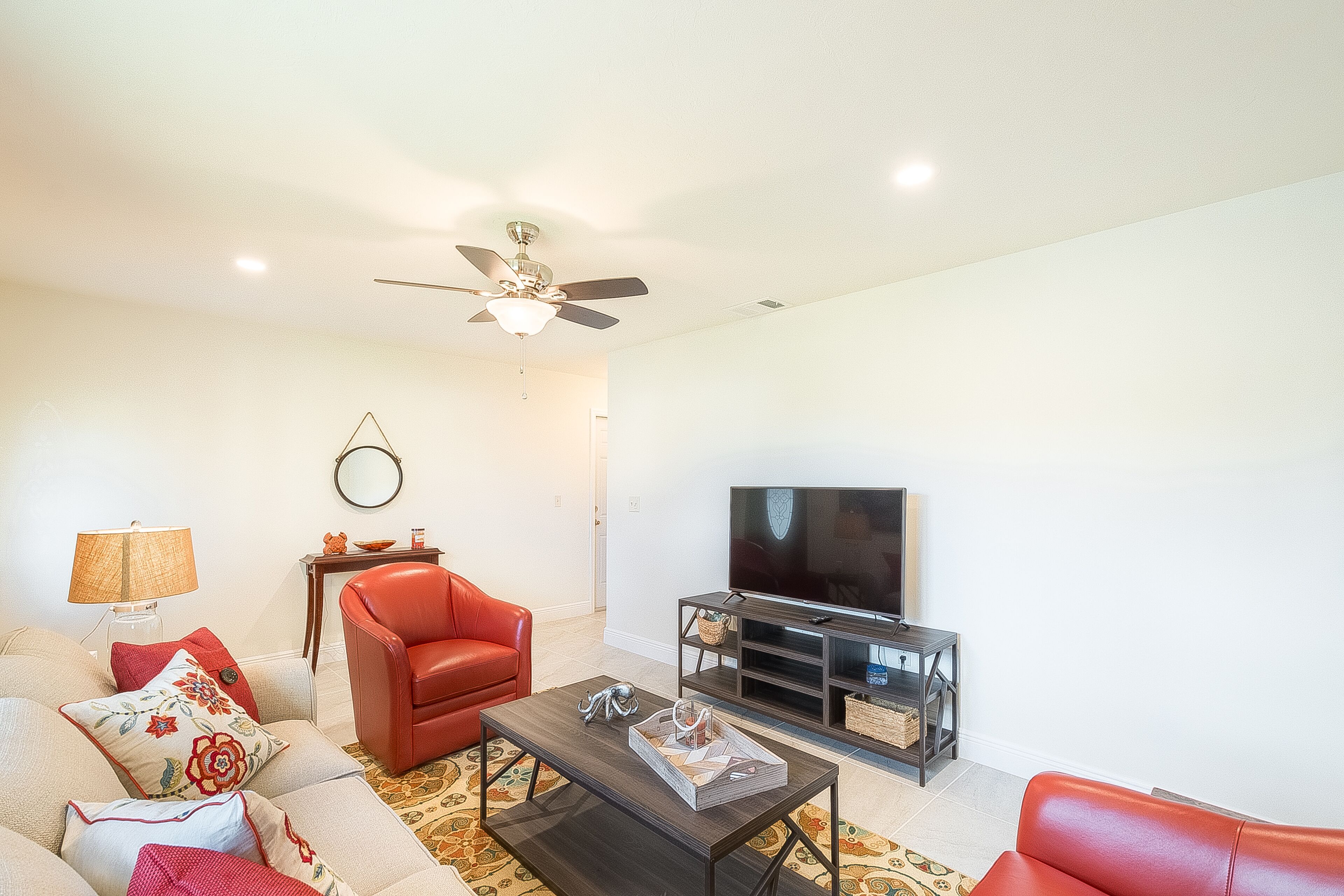 A living room with a sofa, armchair, coffee table, TV stand, and ceiling fan.