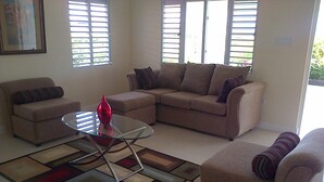 A living room with beige sofas, a glass coffee table, and a patterned rug. - Island Treasure Villa (St. Ann, Ocho Rios)